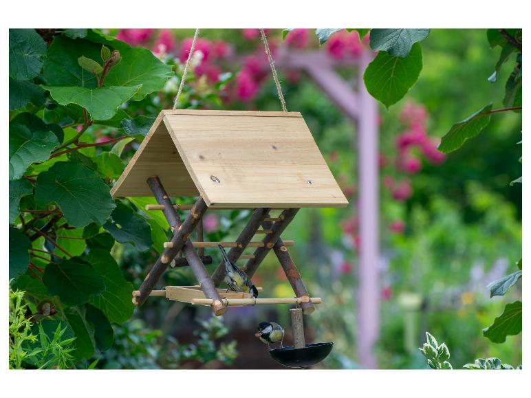 Houten vogelvoederhuisje met twee mezen in een tuin.