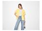 Vrouw in geel overhemd, wit T-shirt en wijde jeans, met strooien tas.