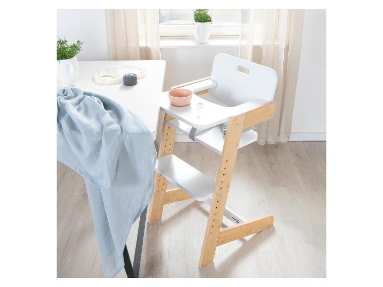 Witte en houten kinderstoel met dienblad, kom en lepel, naast een witte tafel.
