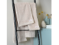 Beige handdoeken hangen aan een zwart ladderrek in een badkamer met lichtblauwe accenten.