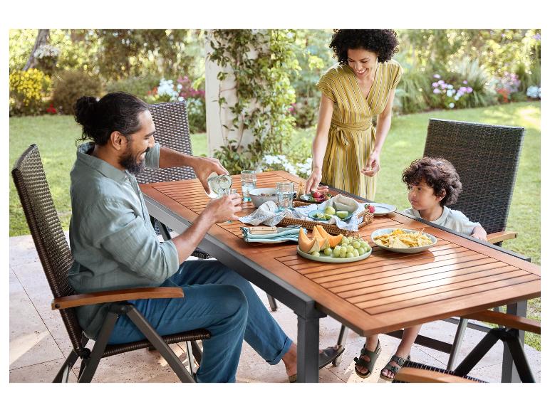 Tuintafel en rotan stoelen; gezin eet buiten.