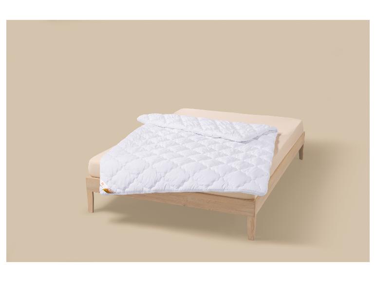 Wit gewatteerd dekbed op een beige matras in een houten bed.