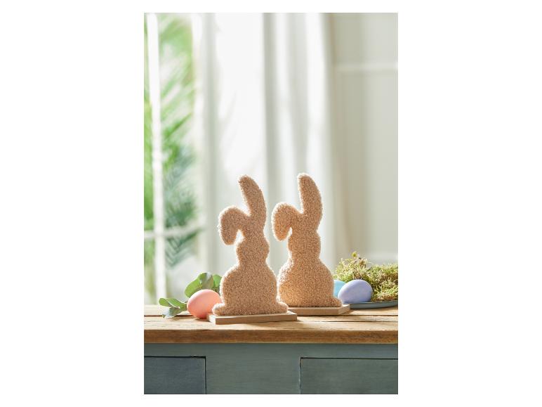 Twee pluche paashazen met eieren op een houten tafel.