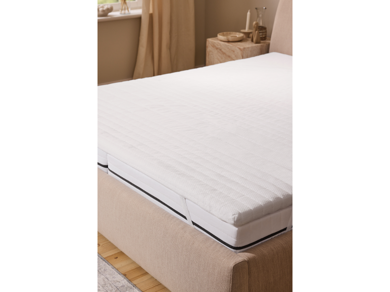 Witte matrastopper op een bed in een neutraal getinte slaapkamer.