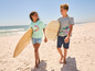 Twee kinderen lopen op het strand met surfplanken.