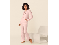 Vrouw in roze hoodie met rits en broek, staand naast een witte fauteuil.