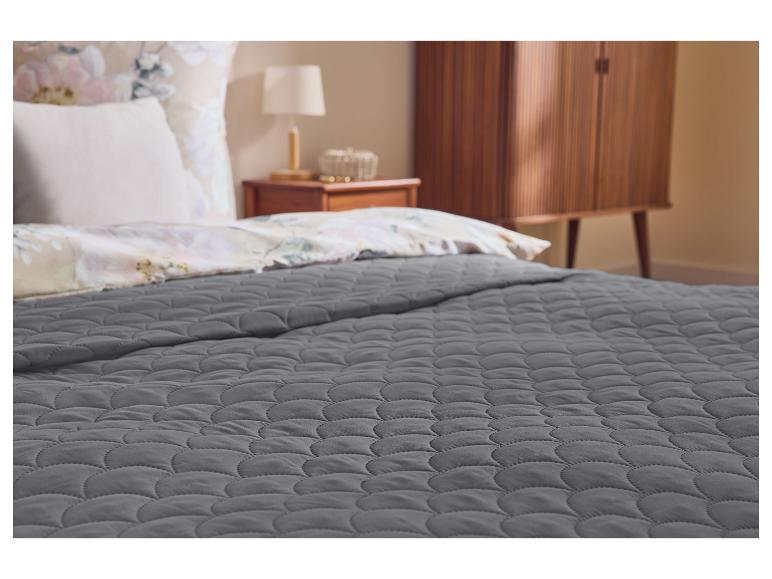 Grijze gewatteerde deken op een bed met bloemenbeddengoed en een nachtkastje