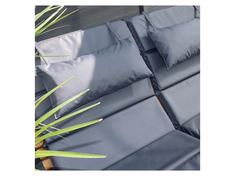 Grijze kussens en kussentjes op een houten ligbed met groene planten.