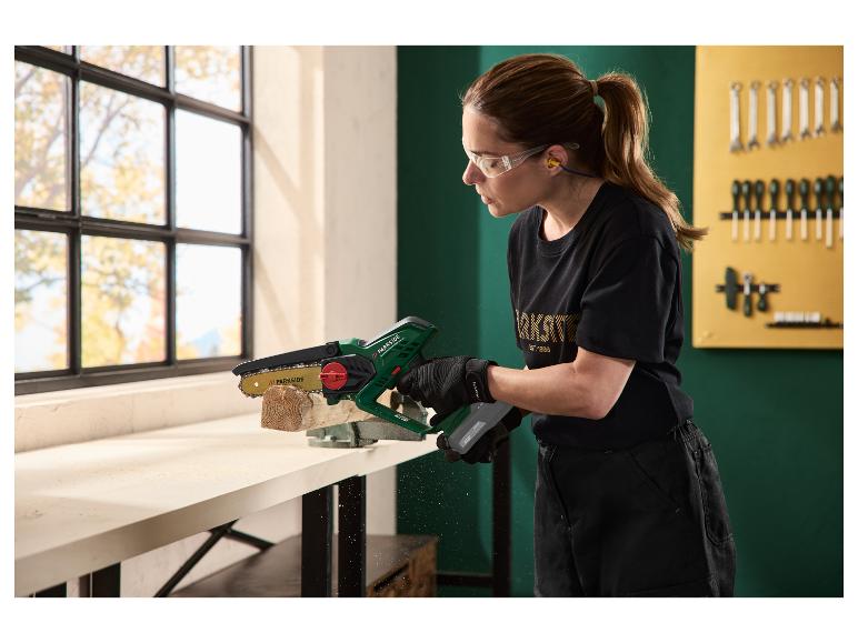 Vrouw zaagt een stuk hout met een mini-kettingzaag, met veiligheidsbril en oordopjes.