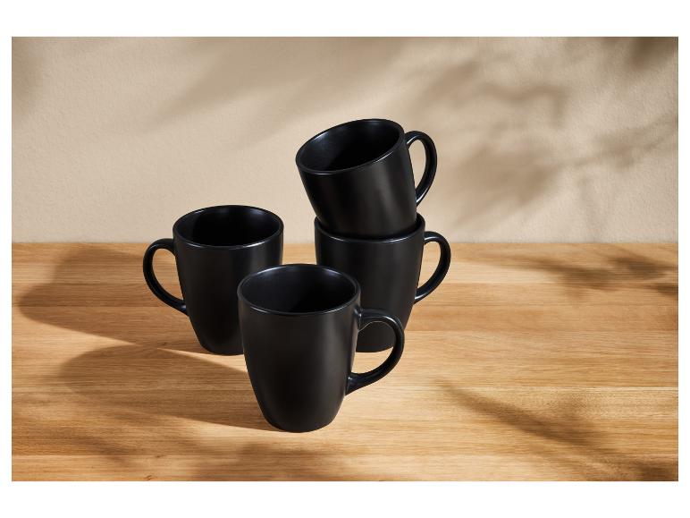 Set van vier matte zwarte mokken op een houten tafel.