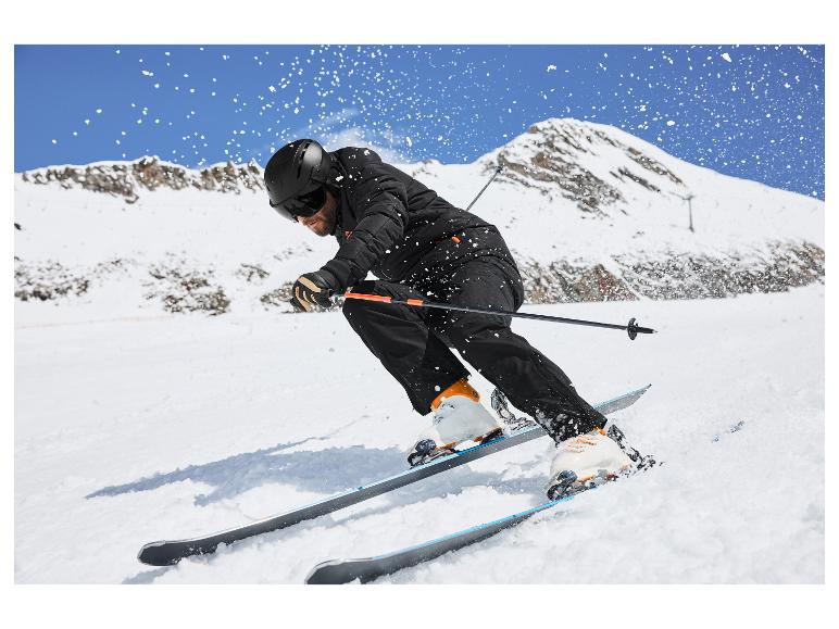 Man skiet van een besneeuwde berg, draagt een zwarte ski-jas, -broek en helm.