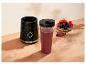 Zwarte blenderbasis met een smoothiebeker en een kom verse bessen op een houten oppervlak.