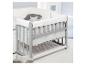 Grijze babywieg met wit beddengoed en decoratieve kussens.