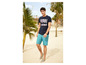 Man in een blauwe T-shirt en turquoise shorts op een strand.
