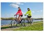 Koppel op e-bikes langs de rivier, gekleed in sportieve jassen en helmen.