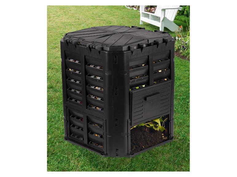 Zwarte compostbak in een tuin met een open onderste klep, die gecomposteerde aarde en bladeren toont.