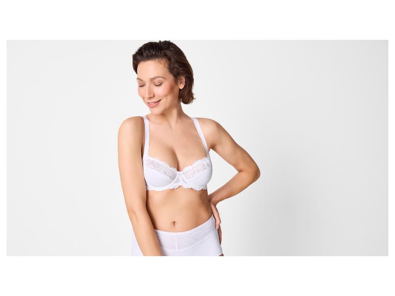 Vrouw in witte beha en slip met kanten details, glimlachend.