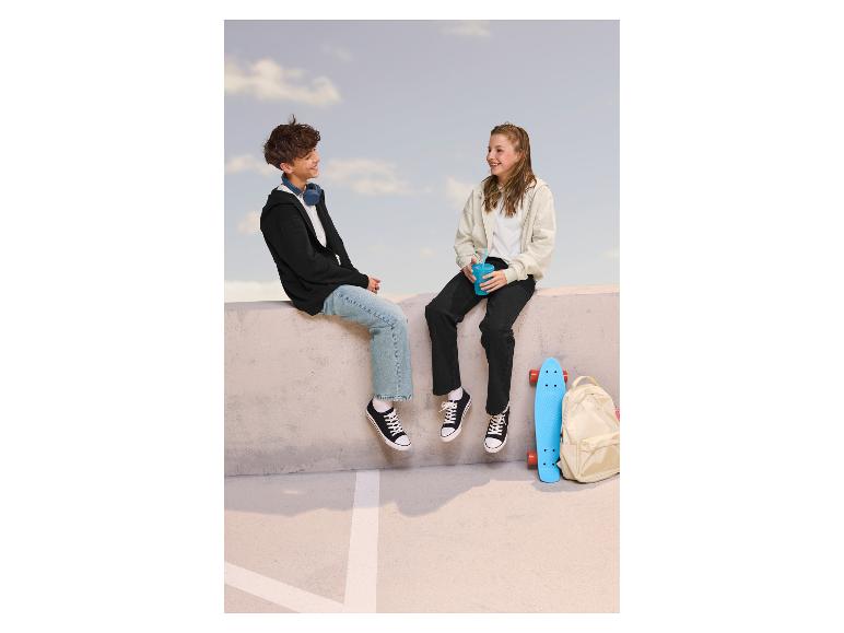 Twee tieners zitten op een muur, dragen hoodies, jeans en sneakers.