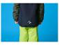 Kind in donkerblauwe en groene ski-jas en lichtgroene skibroek.