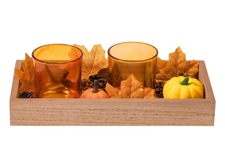 Herfstdecoratie met twee oranje theelichthouders, bladeren, dennenappels en pompoenen in een houten bak.