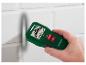 Groene en zwarte multifunctionele wanddetector, vastgehouden door een hand, op een witte muur.