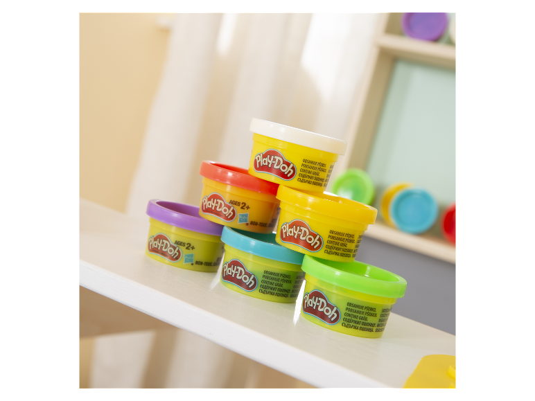 Verschillende gekleurde Play-Doh klei bakjes op een witte tafel.