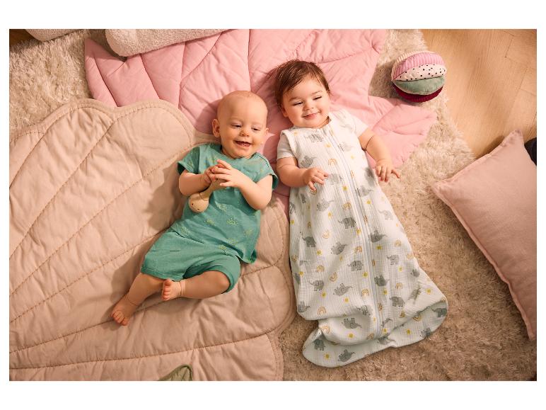 Twee blije baby's op zachte speelmatten, de ene in een slaapzak, de andere in een romper.