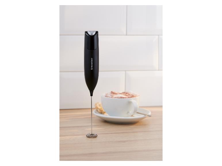 Melkopschuimer naast een kop koffie met schuim op een houten ondergrond.