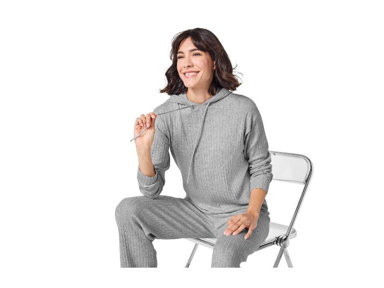 Lachende vrouw in grijze geribbelde hoodie en bijpassende broek, zittend op een stoel