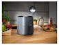 Grijze airfryer in een keuken met verse groenten en fruit in een mand.