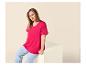 Vrouw in fuchsia T-shirt en blauwe jeans, zittend op een wit blok.