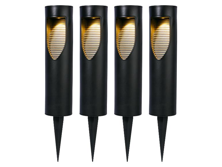 Vier zwarte tuinlampen met grondspies, die warm geel licht uitstralen.