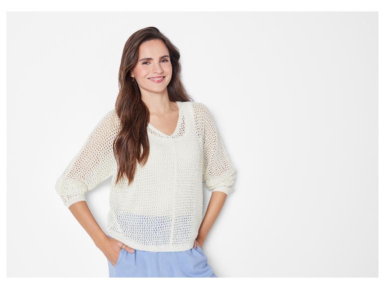 Vrouw in een wit opengewerkt trui en lichtblauwe broek.