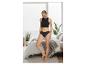 Vrouw in zwarte crop top en slip, staand in een slaapkamer met een groot raam.
