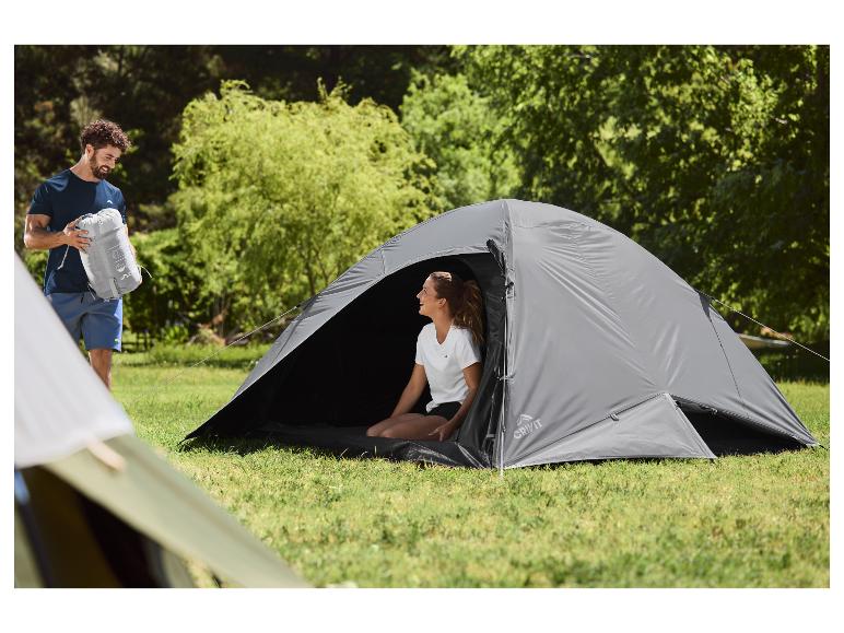 Man met kampeertas en vrouw in tent op grasrijke camping.