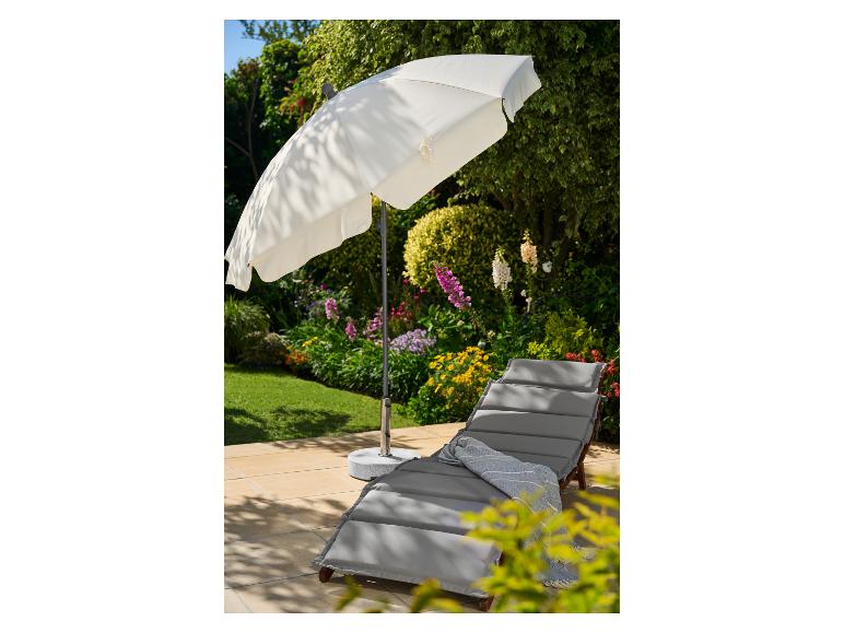 Witte tuinparasol en grijze ligstoel met een blauwe plaid op een terras.