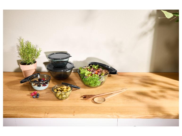 Glazen kommen met deksels, salade, yoghurt met bessen, olijven en kruiden op houten aanrecht.