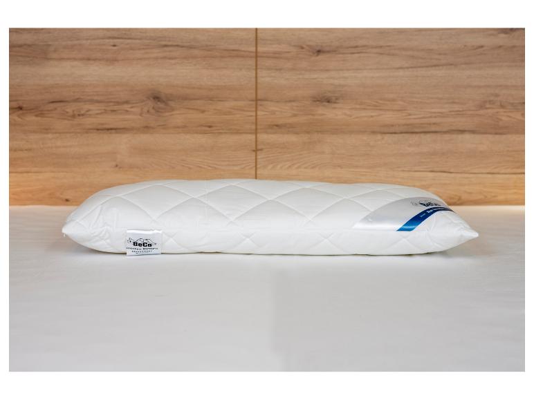 Een wit gewatteerd kussen met merklabels op een bed, met een houten muur op de achtergrond.