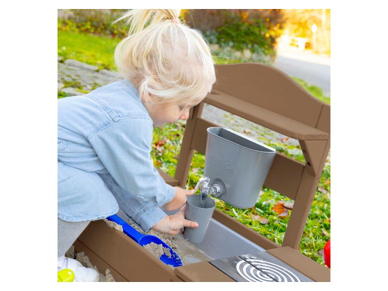 Blond meisje speelt met een houten zand- en waterkeuken, vult een beker met water.