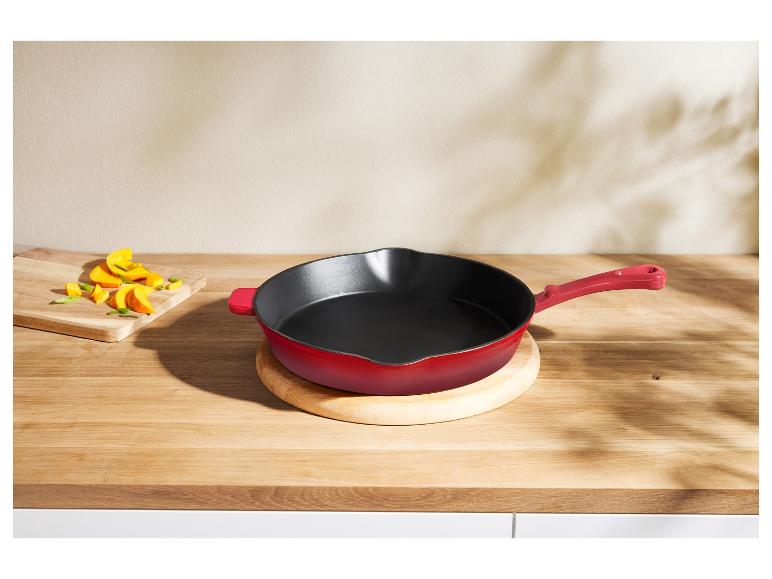 Rode Le Creuset gietijzeren koekenpan op een houten aanrecht.