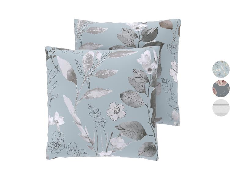 Twee lichtblauwe sierkussens met grijze en witte bloemmotieven.