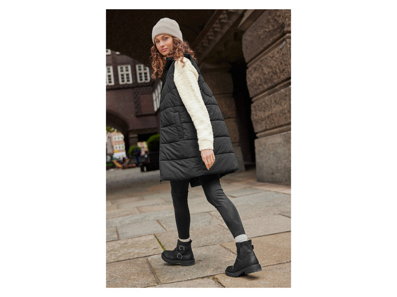 Een vrouw draagt een zwarte gewatteerde vest, zwarte broek en zwarte laarzen.
