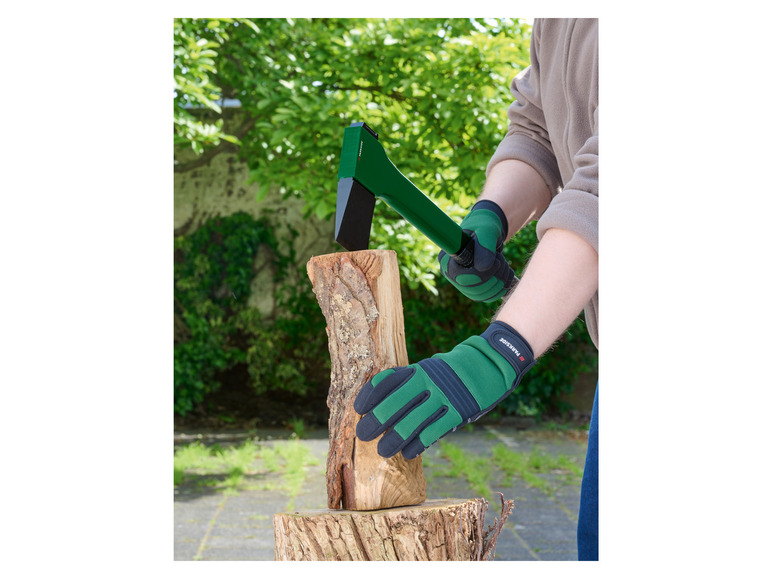 Een persoon gebruikt een groene bijl om hout te hakken met Parkside handschoenen.