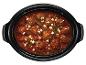 Een slowcooker met meatballs in tomatensaus, feta en peterselie.