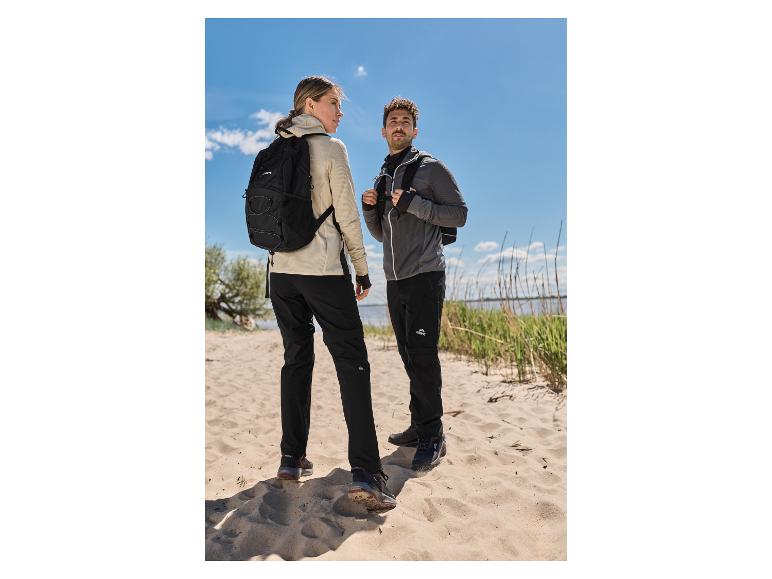 Een vrouw in een beige CRIVIT premium functionele jas en een man die wandelen op een zandstrand.