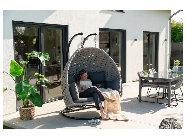Vrouw ontspant in een hangstoel op het terras met een eettafelset.