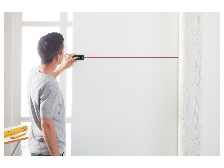 Man gebruikt een laserwaterpas om een horizontale lijn op een witte muur te projecteren.