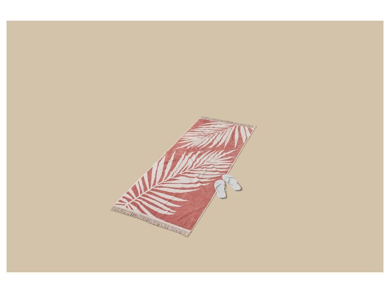 Strandlaken met palmbladprint en teenslippers op een beige achtergrond.
