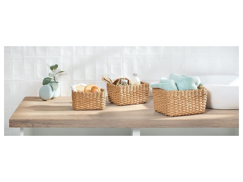 Drie gevlochten manden met badkameraccessoires en handdoeken op een houten aanrecht.