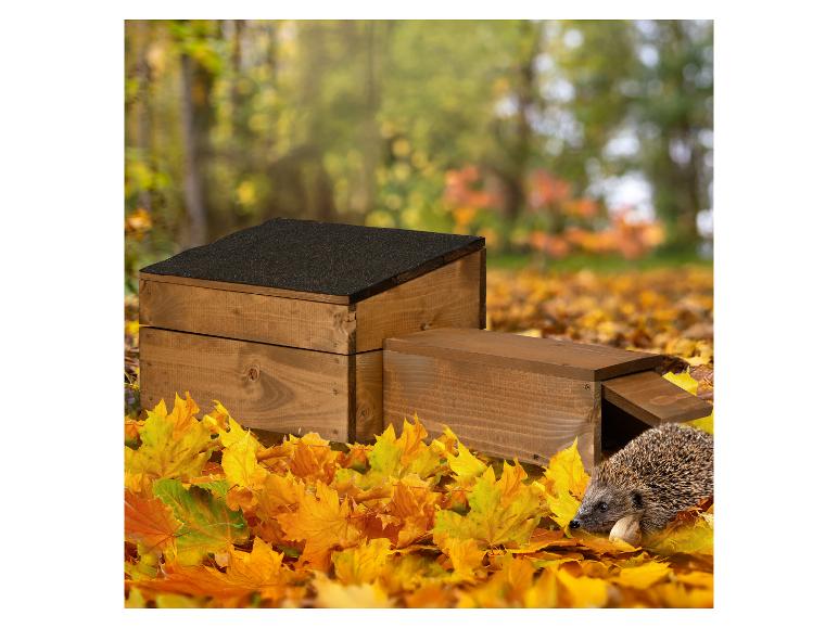 Houten egelhuisje in herfstbladeren met een egel.